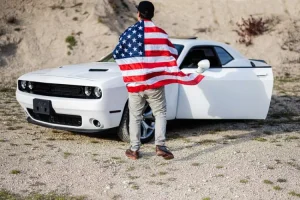 Homme avec un drapeau américain devant une Dodge Challenger